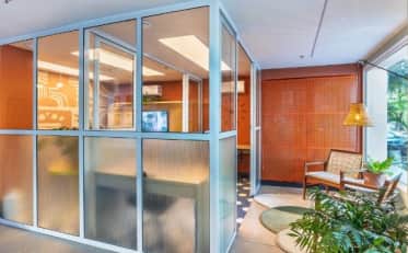 Modern B&B HOTEL lobby featuring a glass-enclosed coworking space and cozy lounge area with plants
