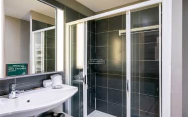 Modernes Hotelbadezimmer im B&B HOME mit schicker Glasduschkabine und dunklen Fliesen
