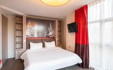 Camera d'hotel moderna con letto matrimoniale, decorazione murale architettonica ed eleganti tende rosse.