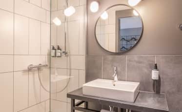 Banheiro de hotel moderno com bancada elegante, espelho redondo e box de vidro com produtos de higiene premium.