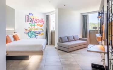 Modern B&B HOME hotel room with king bed and cozy sofa area featuring artistic wall mural and bright contemporary decor