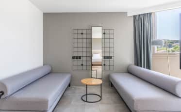 Modern B&B HOME hotel suite lounge area with two grey sofas and a wooden coffee table near a bright window