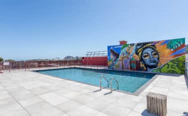 Piscina no terraço de um hotel moderno com mural colorido e vista panorâmica da cidade.