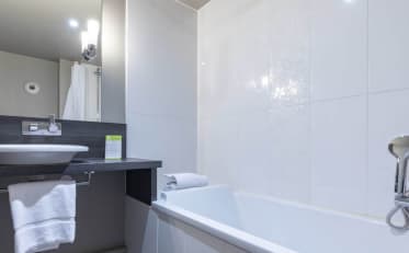 Salle de bain moderne d'hôtel B&B HOME avec baignoire blanche épurée et espace vasque élégant avec serviettes propres