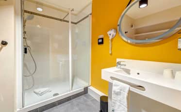 Banheiro de hotel moderno no B&B HOME com box de vidro e detalhes em amarelo vibrante nas paredes