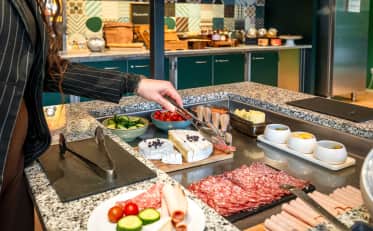 Ospite che si serve al buffet della colazione dell'hotel B&B HOME con salumi e formaggi