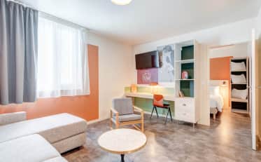 Modern family hotel suite with a cozy sitting area, desk, and a separate bedroom with comfortable bedding.