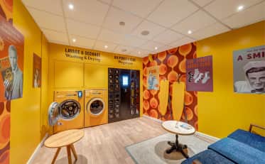 Colorata lavanderia dell'hotel B&B HOME con moderne lavatrici e asciugatrici a disposizione degli ospiti