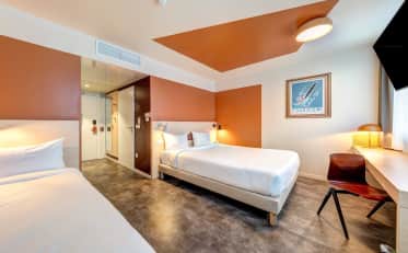 Modern hotel room with two comfortable beds, minimalist decor, and a dedicated workspace with a wooden desk.