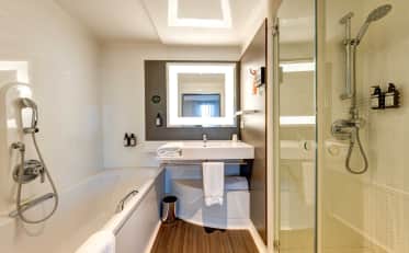 Modernes Hotelbadezimmer im B&B HOME mit Badewanne und separater Glasdusche sowie hochwertigen Pflegeprodukten