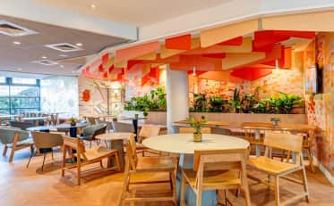 Moderner Frühstücksbereich im B&B HOME Hotel mit bunter Deckenbeleuchtung und Holzmöbeln in einem hellen Speisesaal