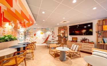 Moderner und farbenfroher Hotel-Loungebereich im B&B HOME mit künstlerischen Wandmalereien und bequemen Holzmöbeln