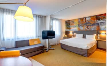 Modernes Hotelzimmer im B&B HOME mit bequemem Kingsize-Bett und gemütlichem Wohnbereich mit Sofa und Flachbildfernseher