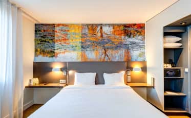 Modernes Hotelzimmer im B&B HOME mit bequemem Doppelbett und künstlerischem Waldwandbild sowie warmer Beleuchtung