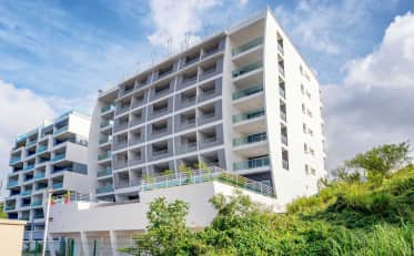 Modern white B&B HOME hotel building facade with balconies and lush green surroundings