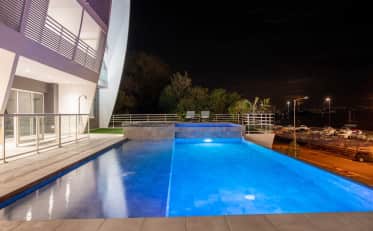 Illuminated outdoor infinity pool at B&B HOME hotel with night view of the marina and modern architecture
