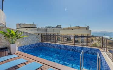 Rooftop swimming pool with blue tiled interior and sun loungers overlooking the ocean