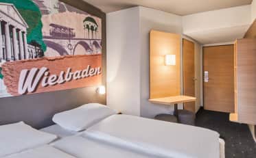 Modernes Hotelzimmer in Wiesbaden mit bequemem Doppelbett und Wandkunst mit lokalem Stadtmotiv.