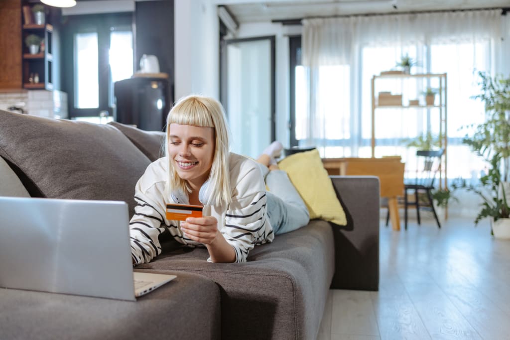 Happy woman on couch holding credit card laying on couch with laptop 