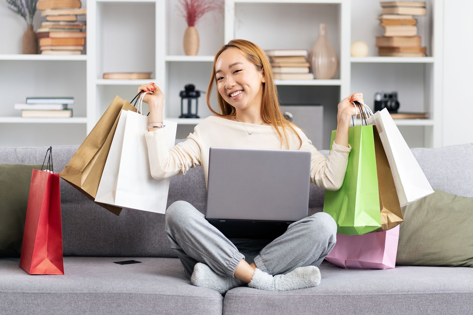 Young woman on couch with shopping bags enjoying online shopping