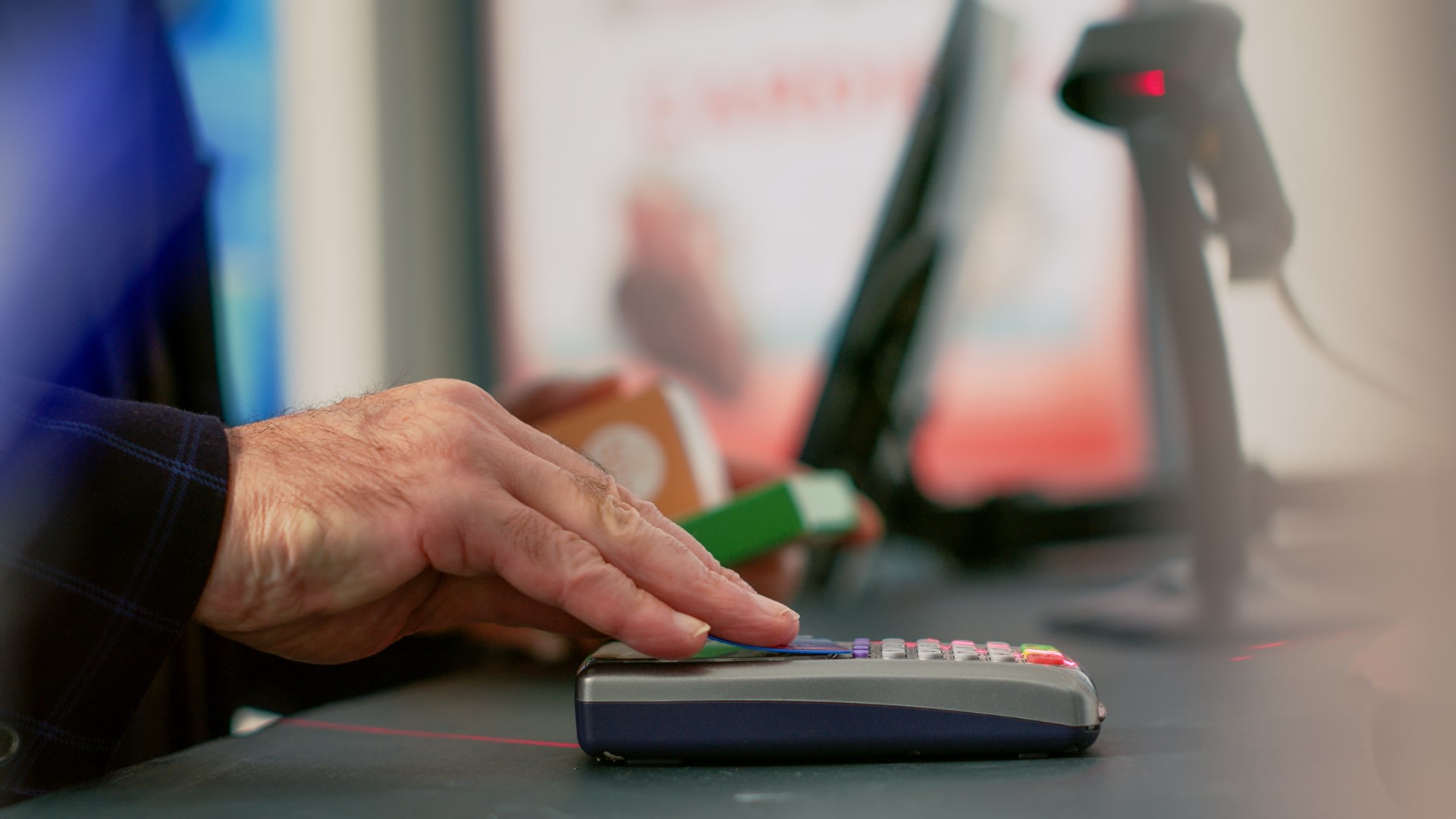 Close-up of a hand tapping a bank card on a contactless payment terminal at a shop counter
