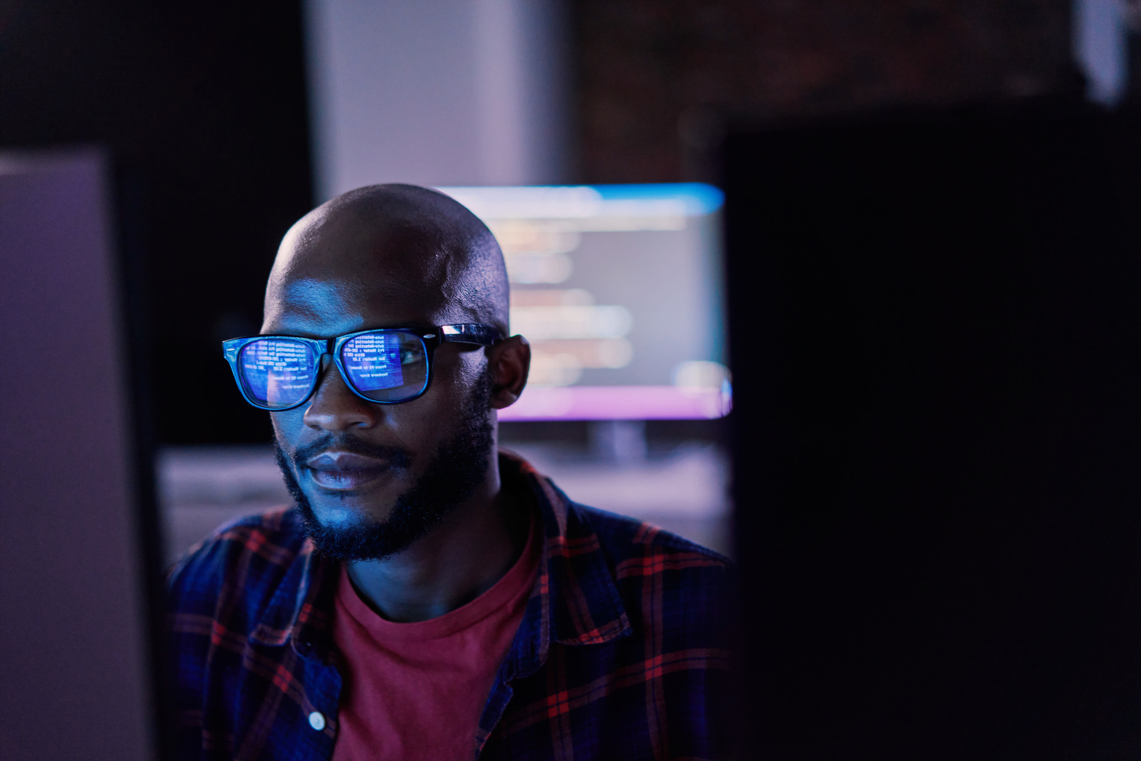 Focused man working at screen with code reflected in his glasses