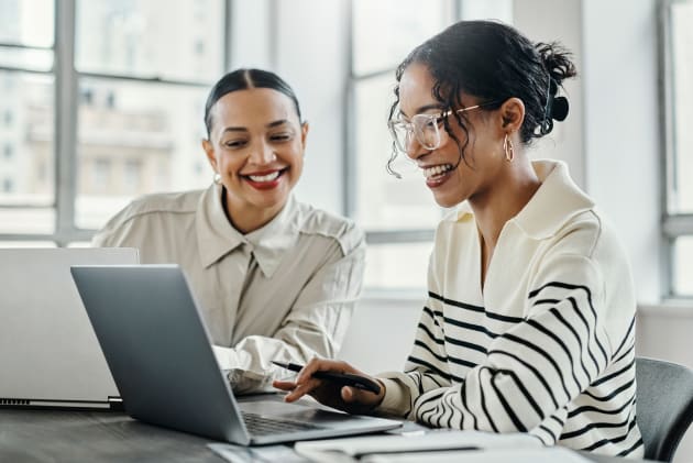Two happy business women conferring over laptop