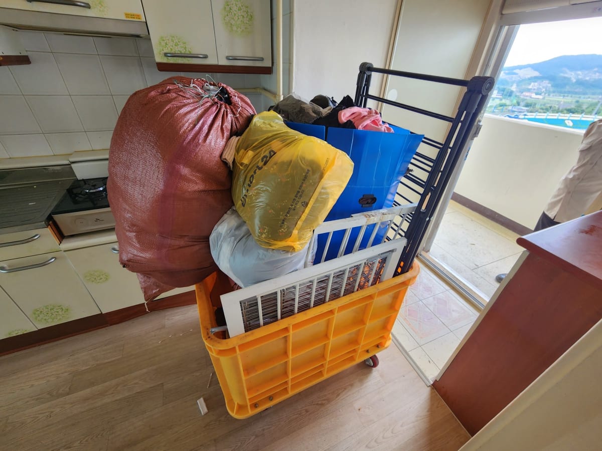 마대와 빨래 건조대를 가득 실은 노란 운반 카트