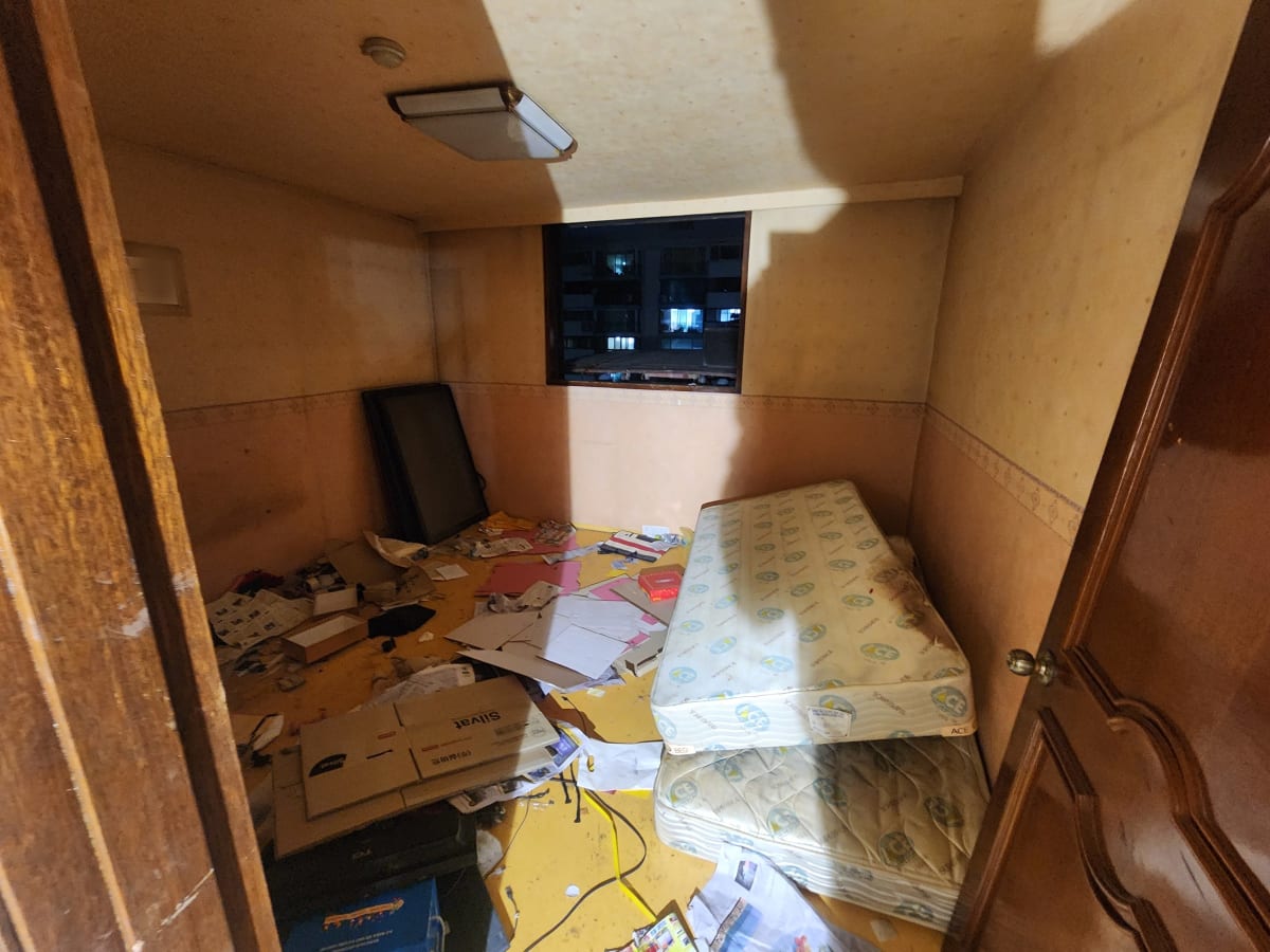 매트리스 두 장과 TV, 바닥에 흩어진 서류와 상자가 쌓인 작은방