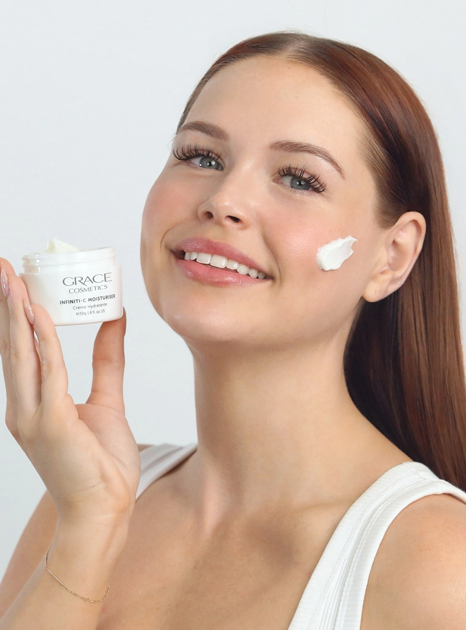Person holding Infiniti-C Moisturiser with product texture on cheek
