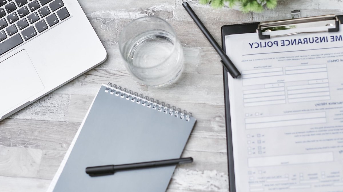 Flat lay of a workspace with a home insurance policy, laptop, and notebook on a desk.