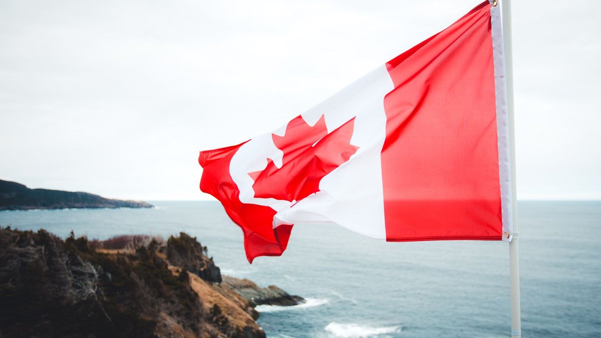 Canadian flag waving over a beautiful, rugged coastline with ocean views.