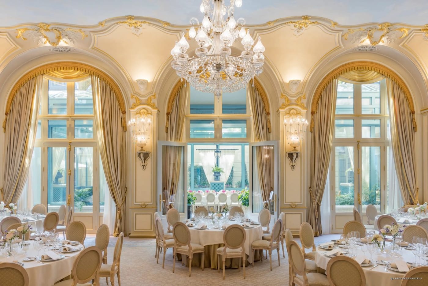 A reception room at the Ritz Paris with chandeliers and large windows overlooking the garden