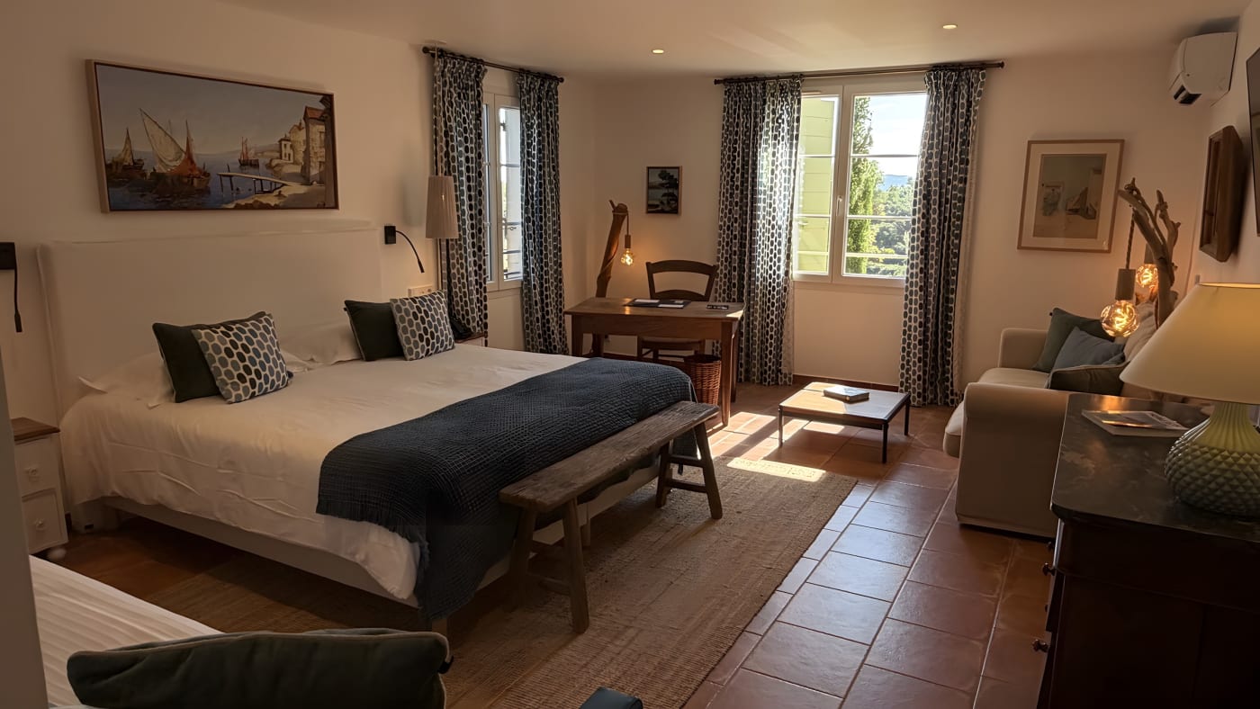 Une chambre de La Ferme d'Augustin à Ramatuelle, grand lit, plaid bleu, tomettes et tableau de voilier