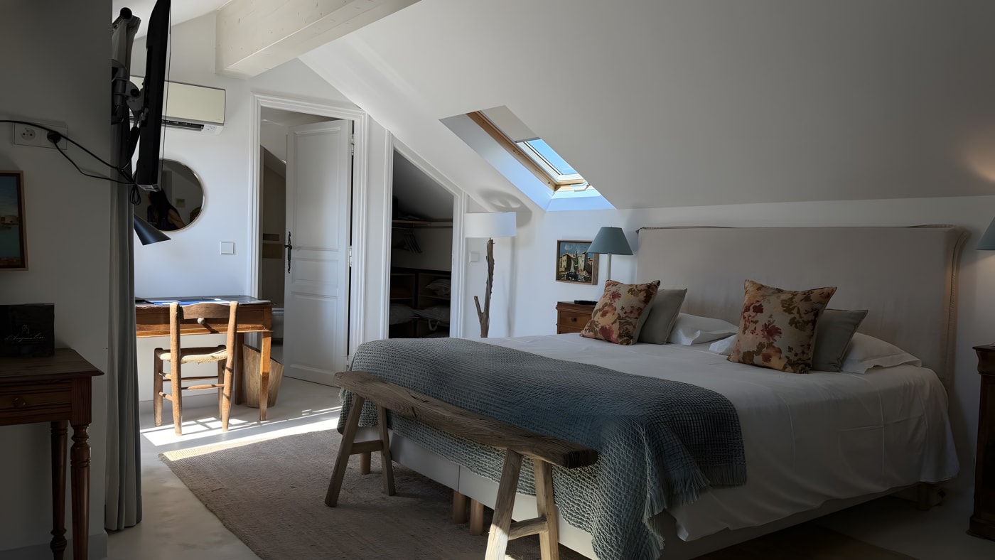 Chambre sous les toits de La Ferme d'Augustin, poutres, velux, lit à coussins brodés et banc