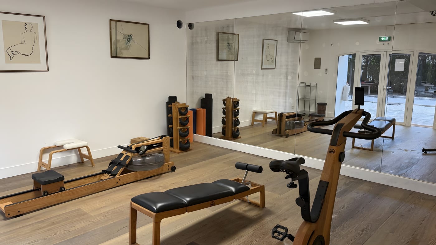 La salle de fitness de La Ferme d'Augustin, rameur et banc NOHrD en bois, vélo et haltères