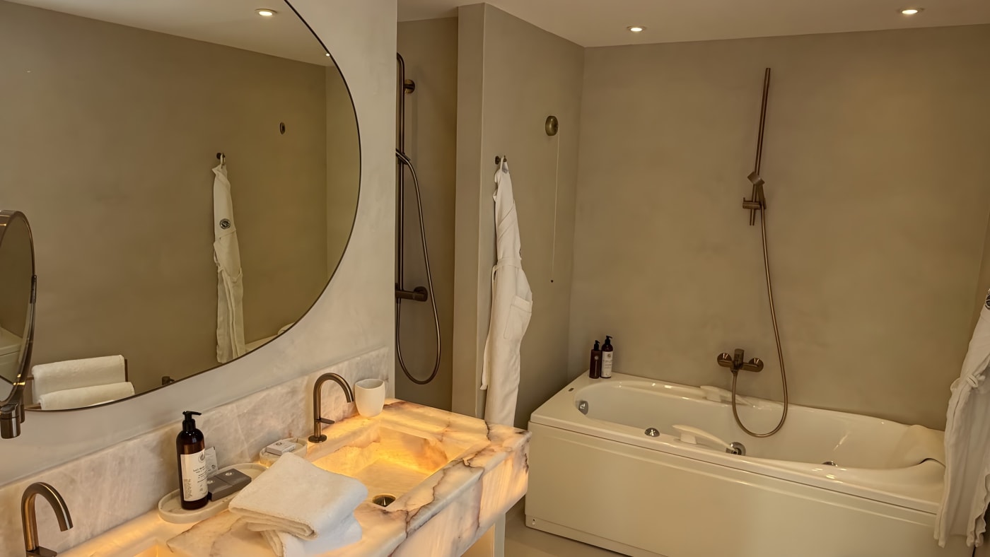 Salle de bains de notre chambre à La Ferme d'Augustin, vasque en marbre rétroéclairé, robinetterie cuivre, miroir arrondi et baignoire balnéo