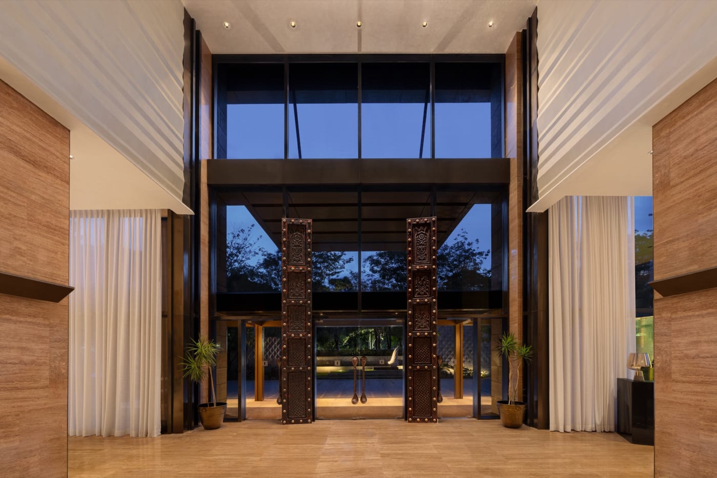 The lobby entrance of The Den Bengaluru, LXR Hotels & Resorts, with carved wooden doors and double-height glazing