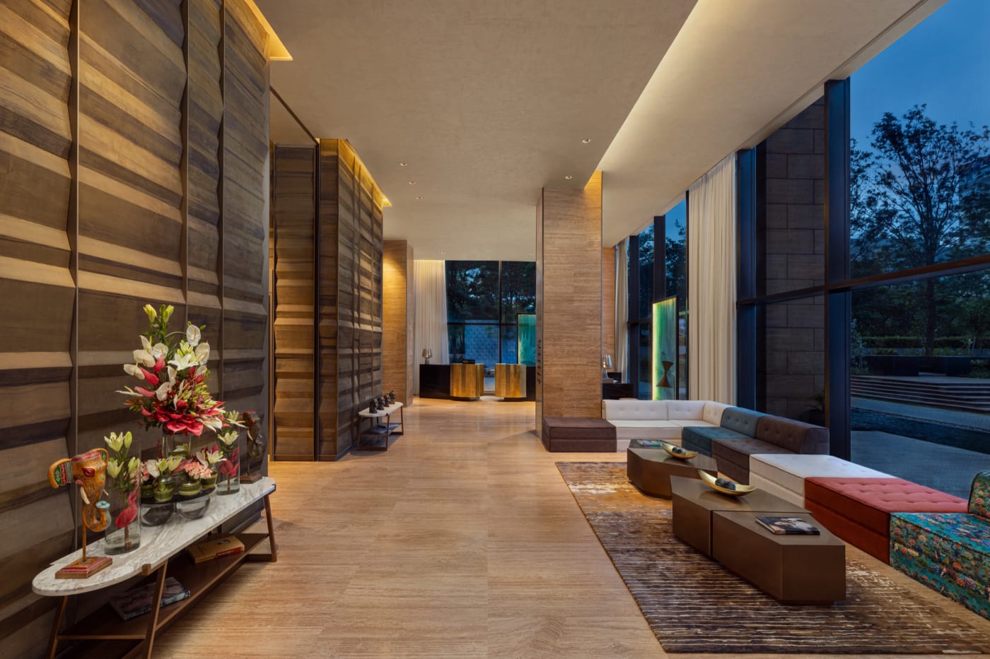 The lobby of The Den Bengaluru, LXR Hotels & Resorts, with fluted wood walls, colourful banquettes and openings onto the garden