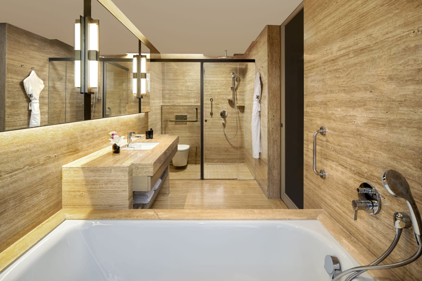 Travertine bathroom with bathtub and walk-in shower in a room at The Den Bengaluru, LXR Hotels & Resorts