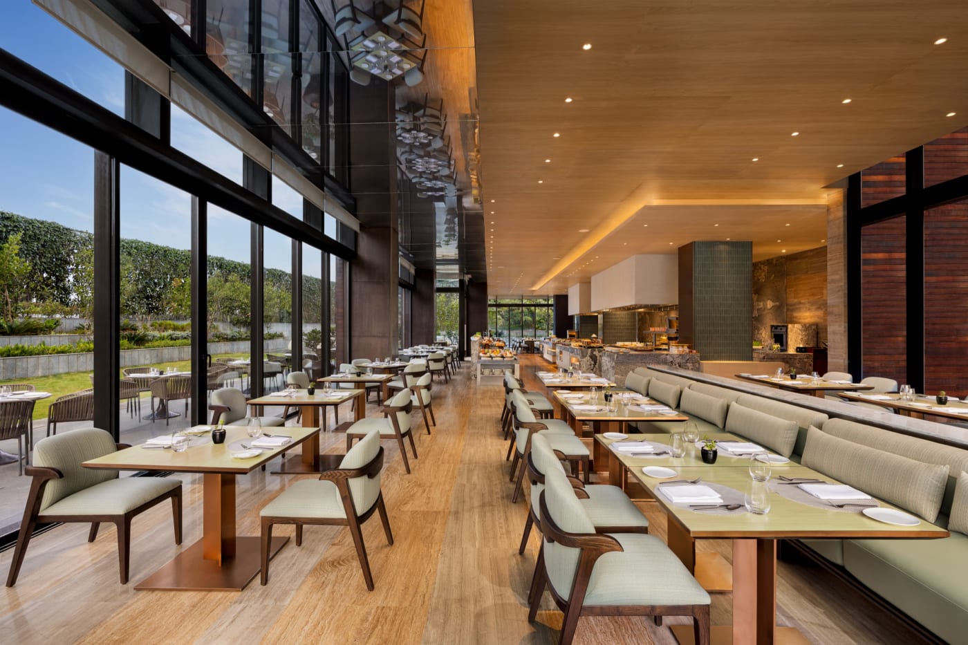 The dining room of The Creek restaurant at The Den Bengaluru, LXR Hotels & Resorts, bathed in light and opening onto the lawn