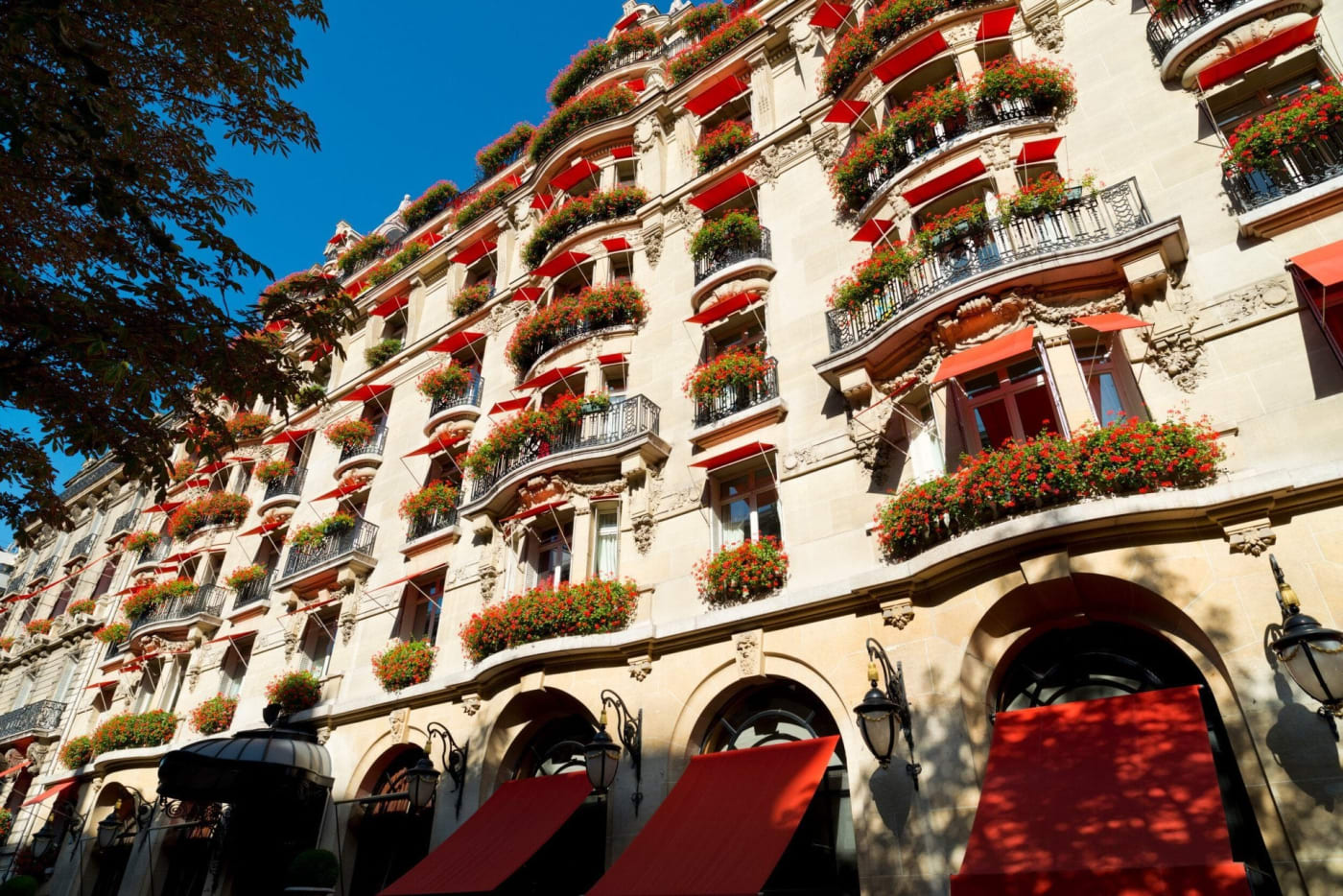 La façade du Plaza Athénée, ses balcons fleuris et ses stores rouges, avenue Montaigne à Paris