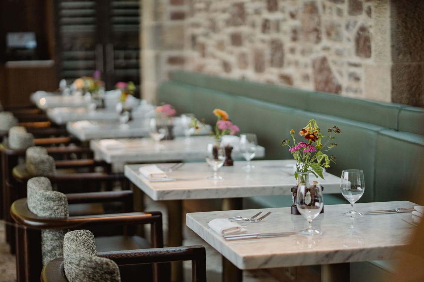 Salle de restaurant de l'hôtel Cromlix, tables en marbre et banquette verte contre un mur de pierre