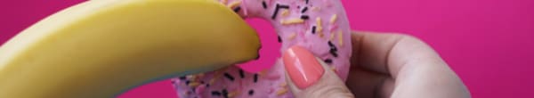 A banana being inserted into a sprinkle donut.