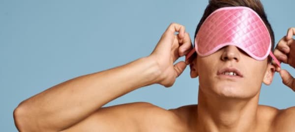 A shirtless muscular person puts on a silk blindfold.