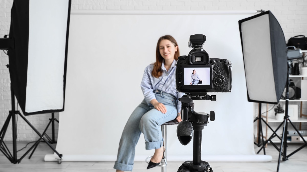 A headshot session in progress: the subject on a stool against white, lit by two softboxes, seen past the camera