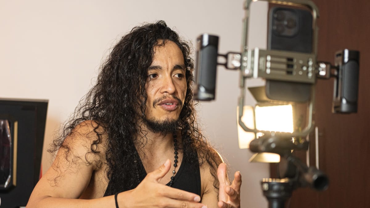 A performer talking to a camera on a tripod with an LED panel beside it, filming indoors