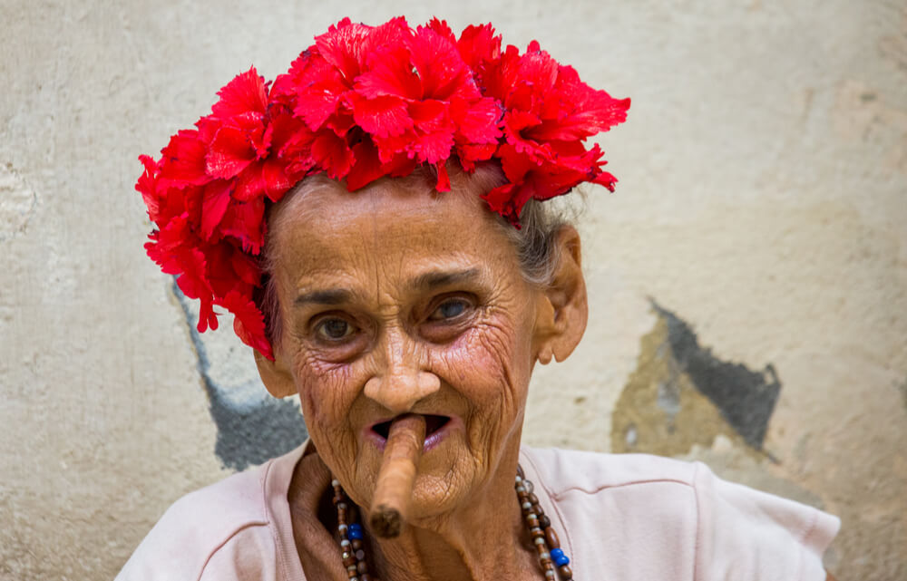 A portrait of an old woman with a cigar sitting on the sidewalk on the street of old Havana, Cuba