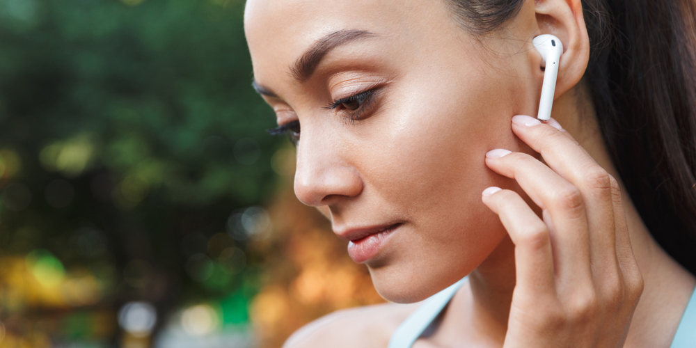 Image closeup of brunette woman in sportswear using bluetooth earbuds