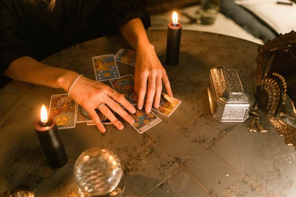 woman spreading tarot cards on table with candles and crystal ball